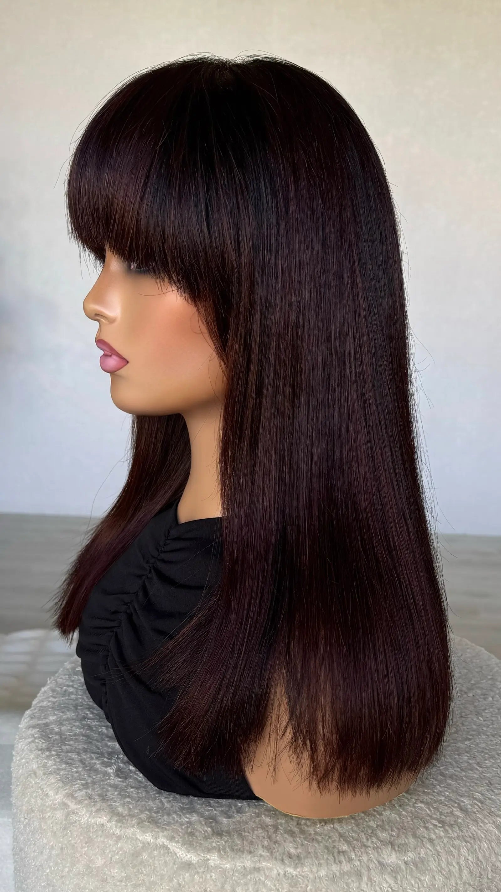 side on view of thick fringe wig with light face framing layer. darkest brown hair with burgundy highlights.