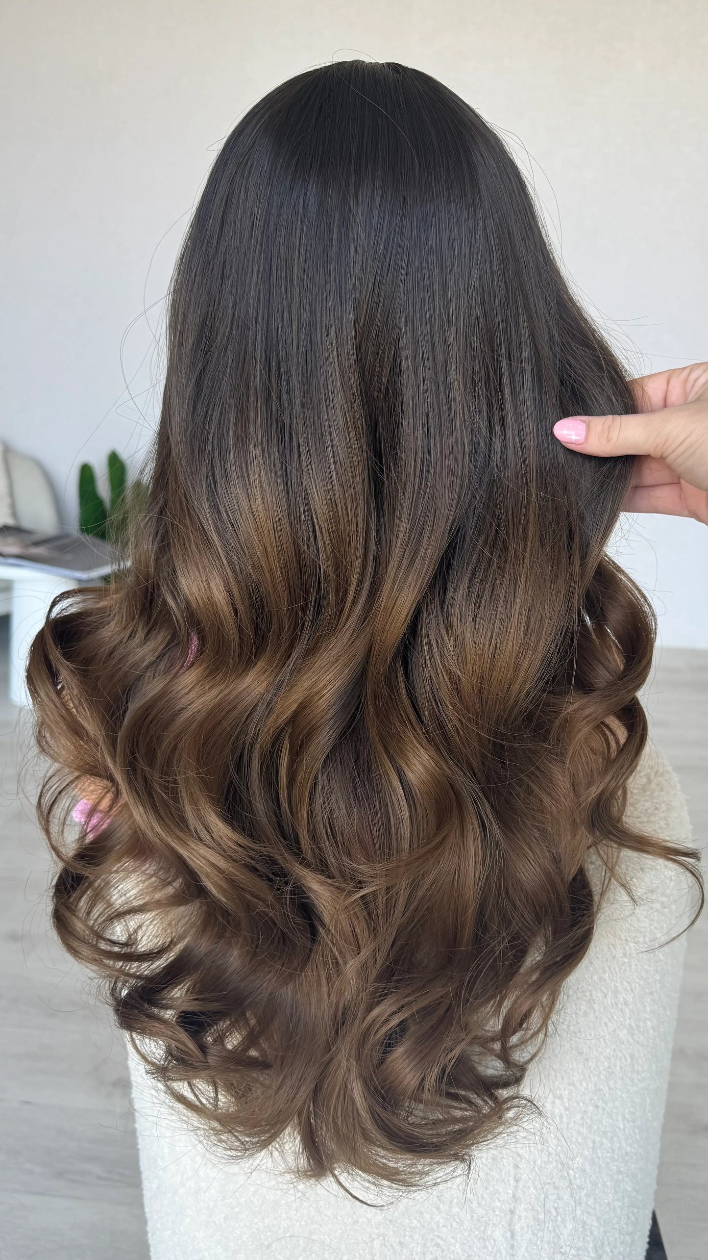 back view holding long wavy brunette hair, heat safe wig.