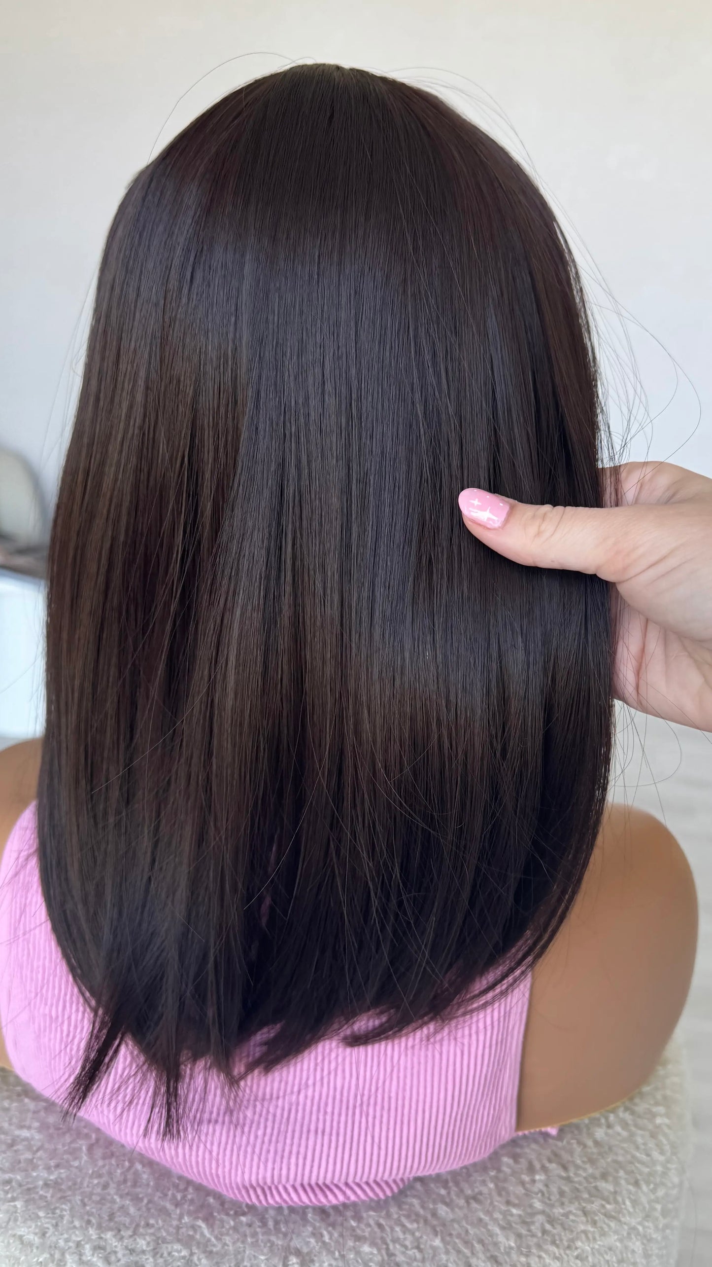 Person holding a long, straight black hair extension against a neutral background