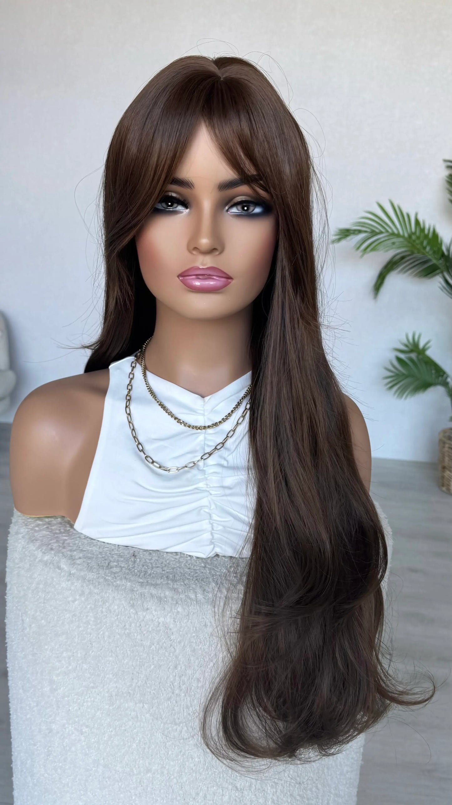 Mannequin head with long brown wig and white top against a neutral background, half hair back.