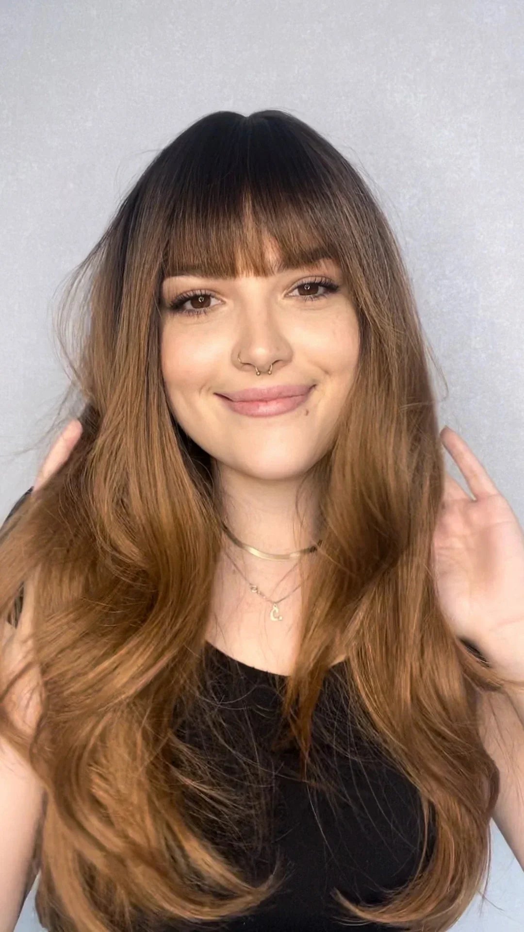 model wear long brunette synthetic wig with fringe. smiling, soft energy wearing a black top.
