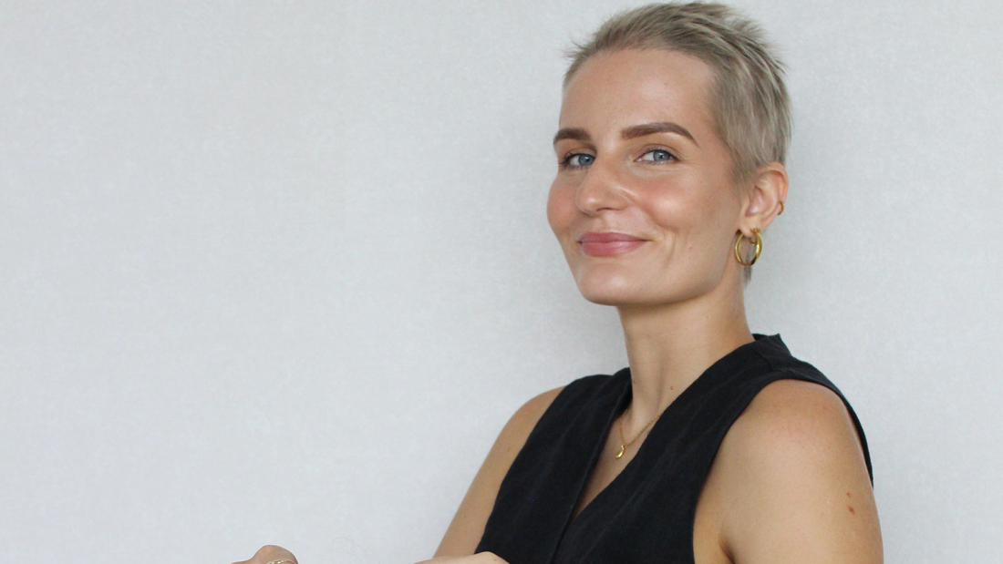 alopecia model smiles at camera with short blonde hair, white back ground, black top