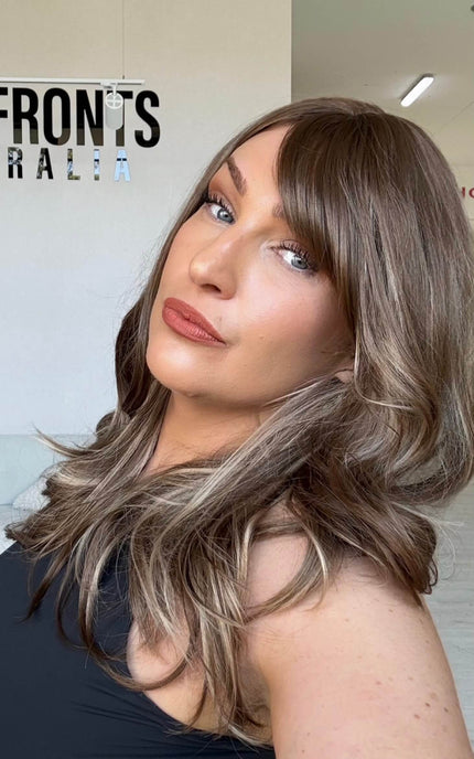 20 inch warm brunette hair with ash and honey blonde highlights, a long fringe parted to the side and light layers throughout.