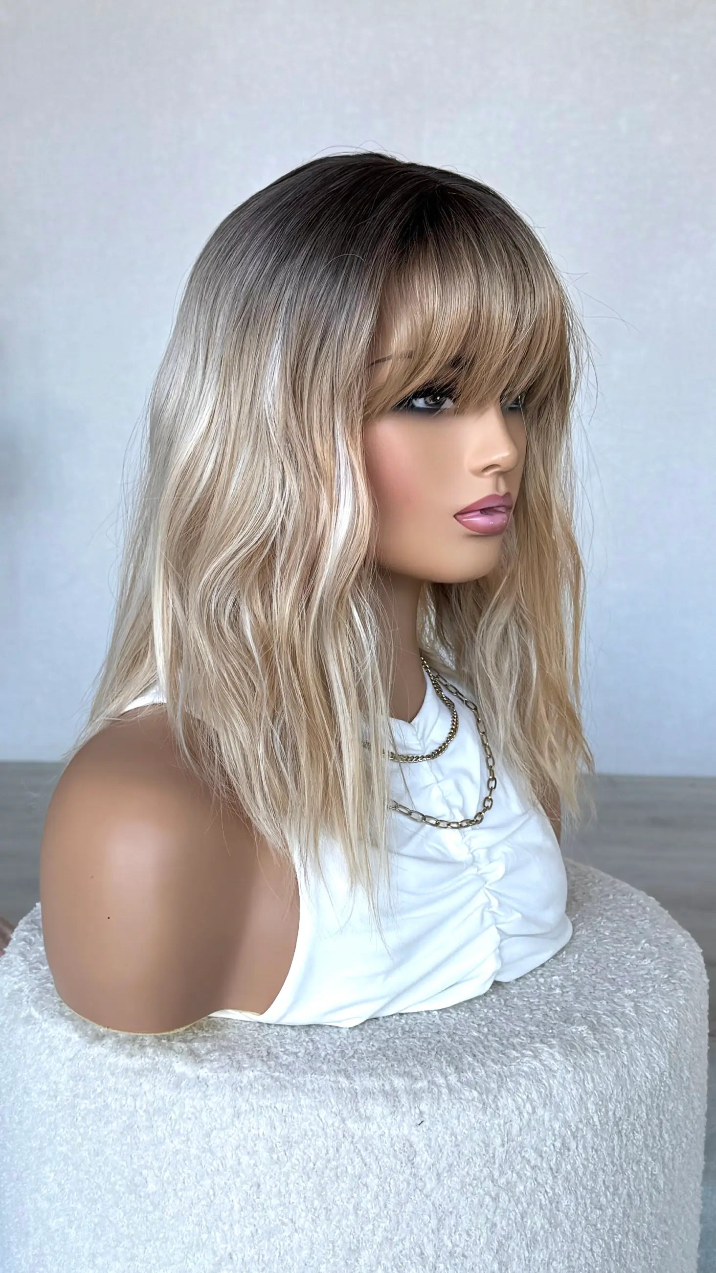 side view, dark root to mixed blonde hair, wavy wig with fringe.