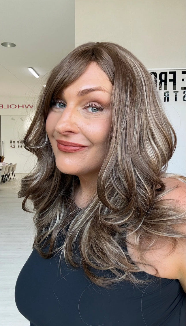 Warm brunette synthetic wig with ash and honey blonde highlights underneath, a middle part, long fringe parted to the side and light layers throughout.