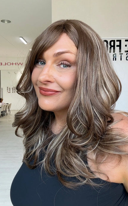 Warm brunette synthetic wig with ash and honey blonde highlights underneath, a middle part, long fringe parted to the side and light layers throughout.