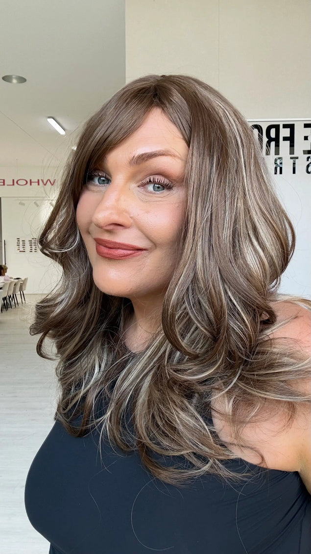 Warm brunette synthetic wig with ash and honey blonde highlights underneath, a middle part, long fringe parted to the side and light layers throughout.