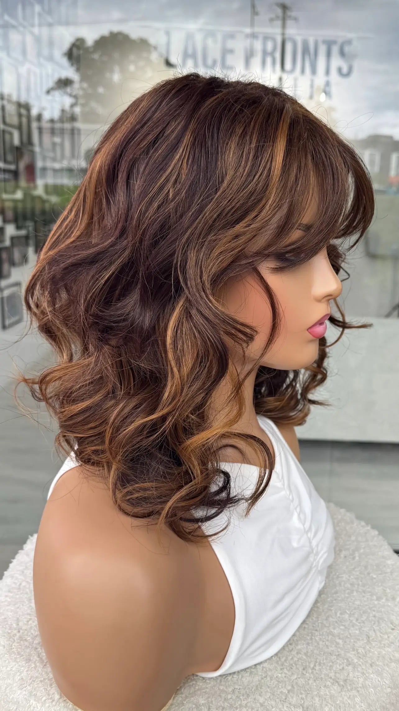 Toffee swirl synthetic wig from the side on. showing curly highlighted hair in natural light.