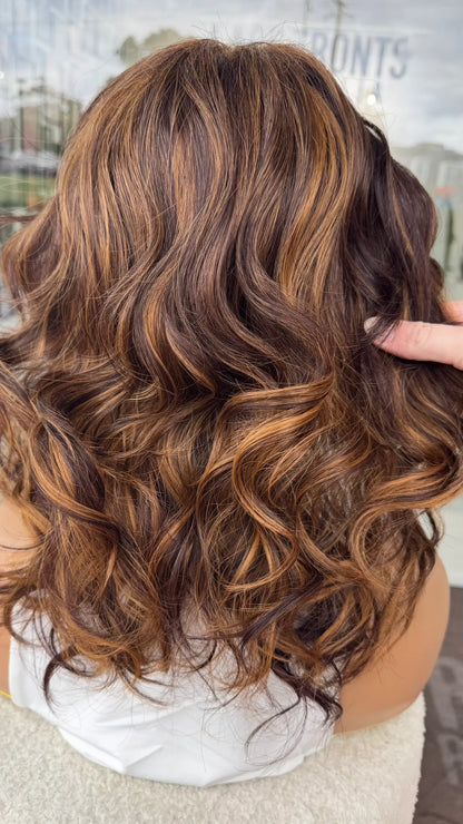 toffee highlights through warm brunette hair. curly hair being held from the back in natural lighting.