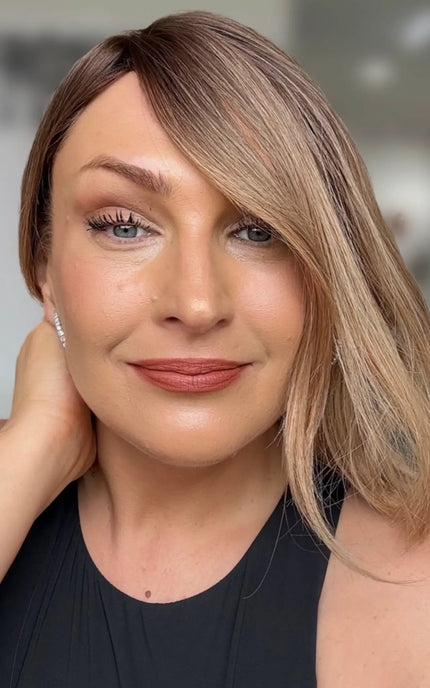 a close up shot of natural looking hairline with face framing layers slightly over one eye, slight side part, with soft brunette root and light curl throughout.
