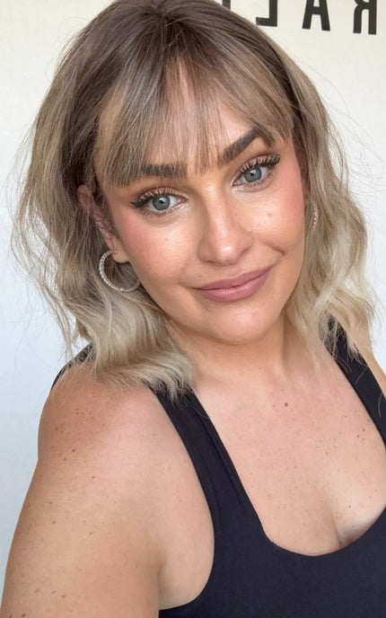 wavy hair synthetic wig, darker root, middle parting with fringe.