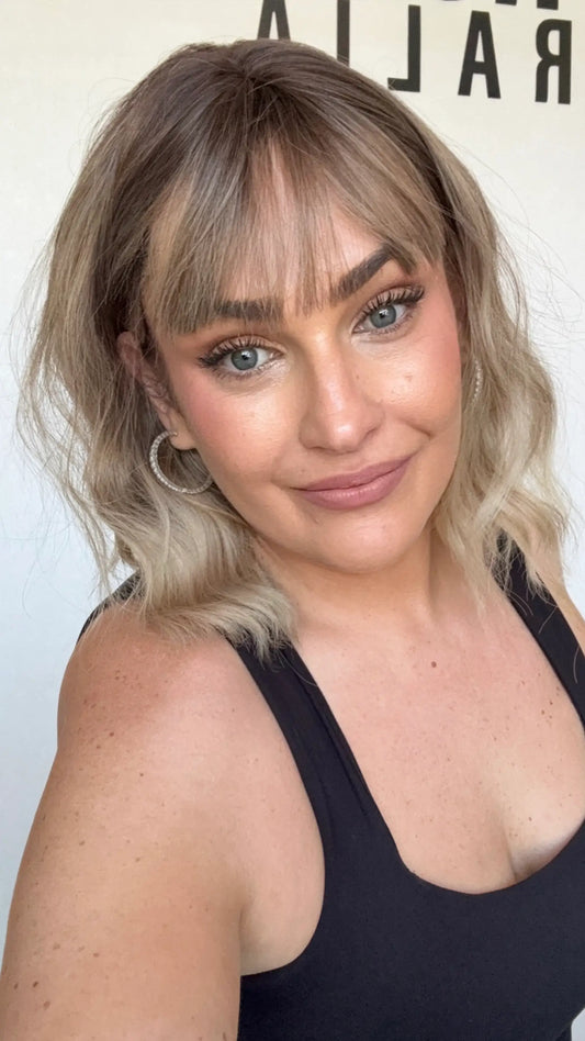 wavy hair synthetic wig, darker root, middle parting with fringe.