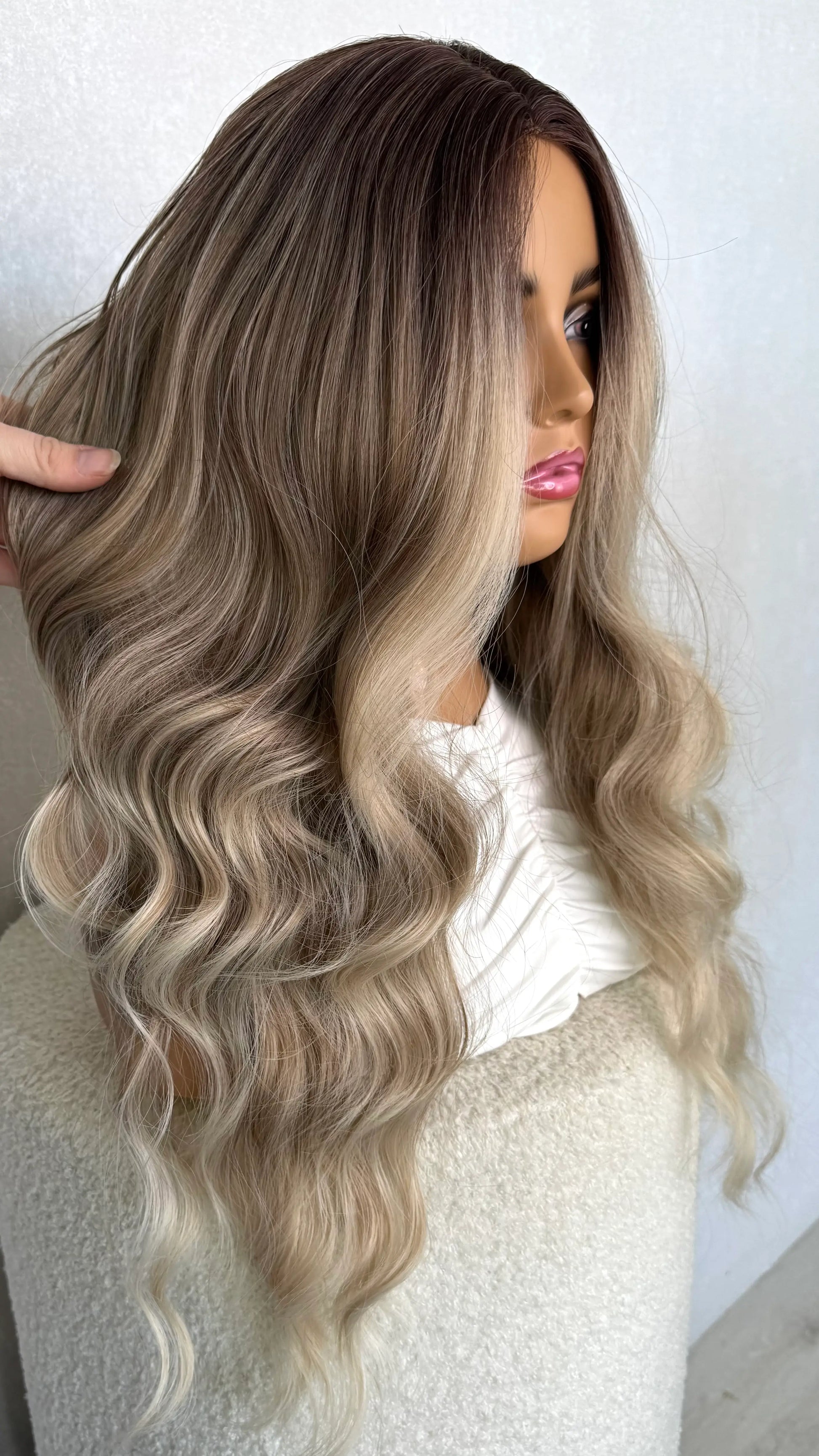 ash blonde synthetic wig from side on. holding the hair to show the natural colour. ash blonde ombre hair.