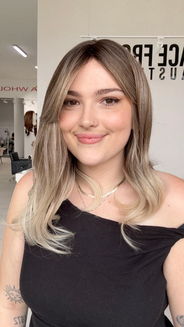 a curled end, mid length ash blonde wig with a middle part, long curtain bang fringe parted to the side, this wig has adjsutable straps and heat safe hair.