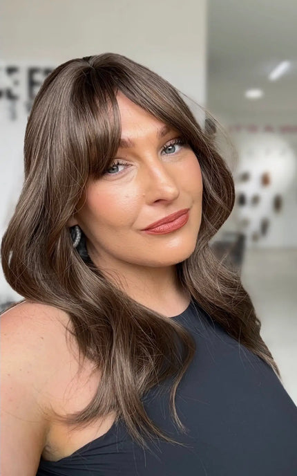 a women wearing a cool toned brunette layered hair wig, with soft curtain bangs and a middle part.