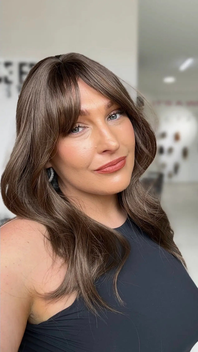 a women wearing a cool toned brunette layered hair wig, with soft curtain bangs and a middle part.