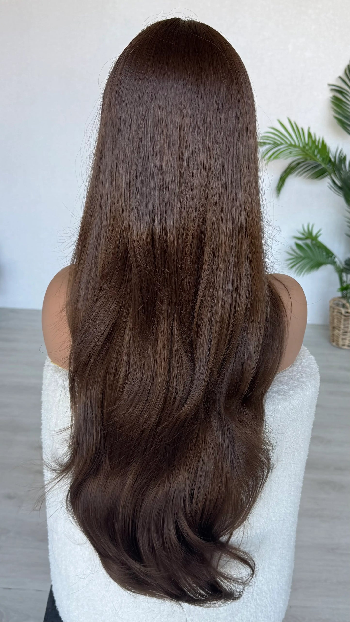 Person with long, straight brown hair sitting on a white chair indoors. australia wigs.