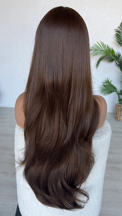 Person with long, straight brown hair sitting on a white chair indoors. australia wigs.