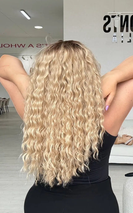 a back view of the mid to long length curly blonde hair with slight brunette shadow root for natural look.