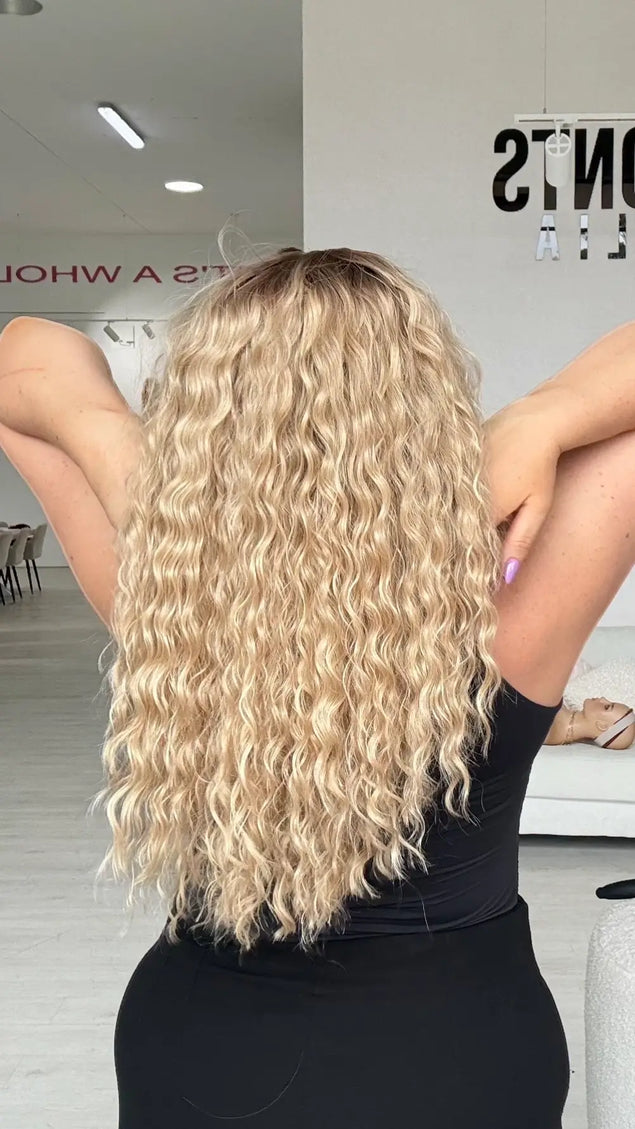 a back view of the mid to long length curly blonde hair with slight brunette shadow root for natural look.