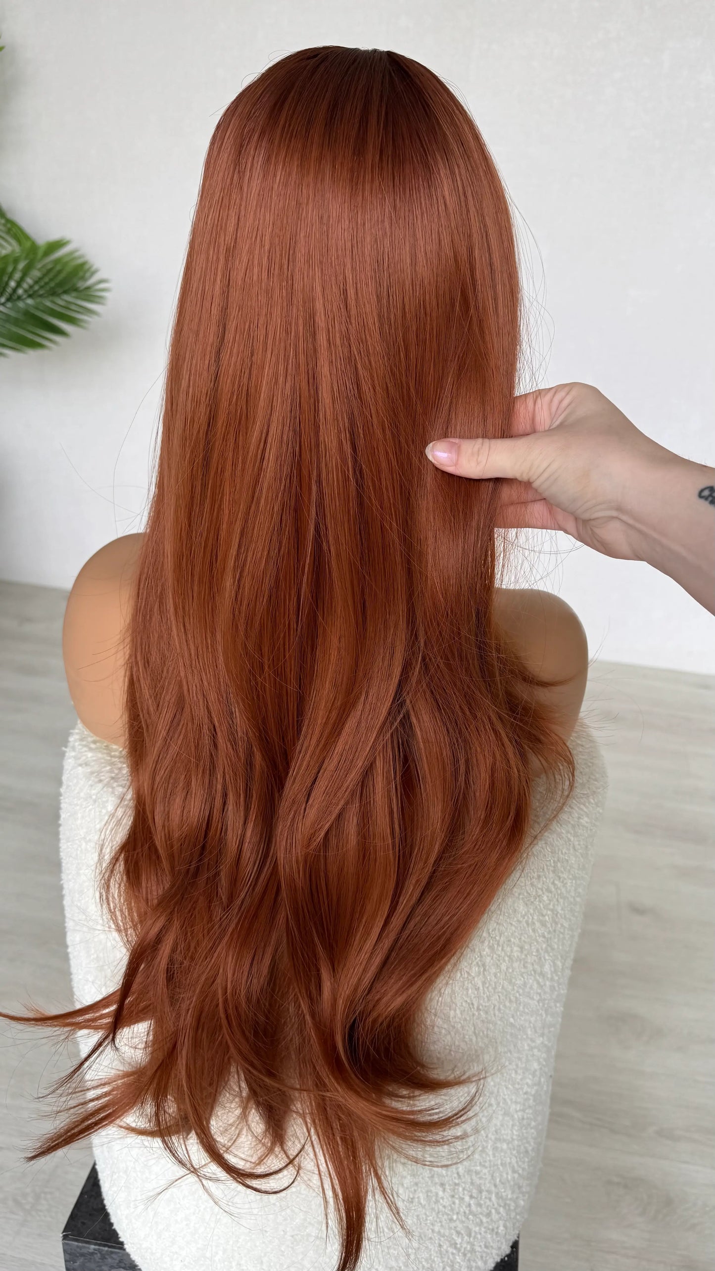 copper hair with darker root, holding the long hair.