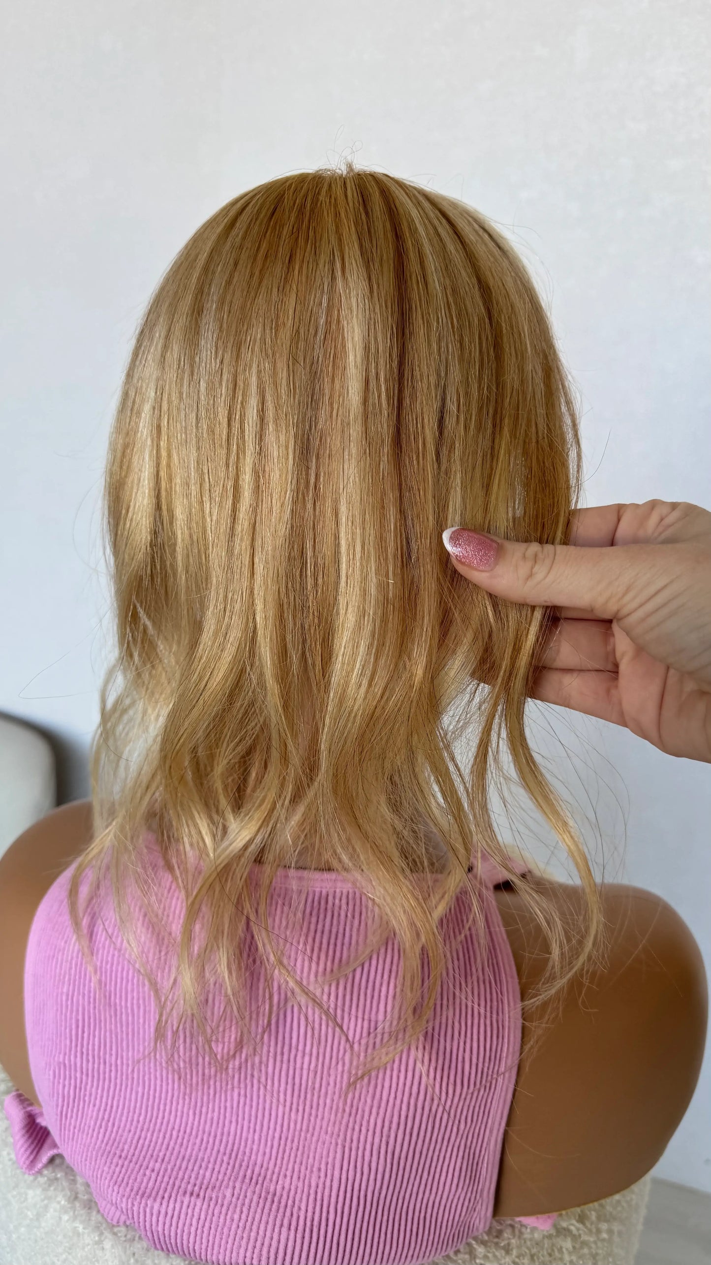 mini 16 inch topper from behind, holding the warm blonde hair.