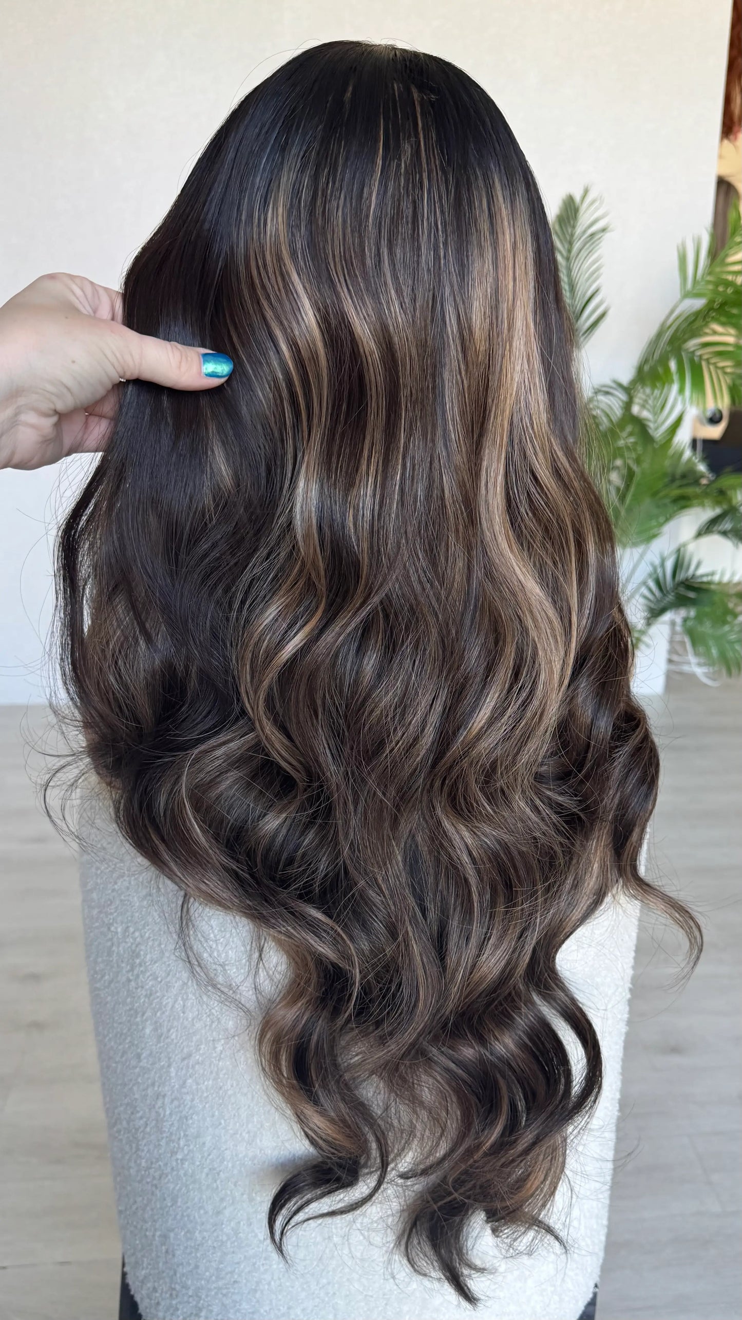 Long, wavy hair with brown and blonde color gradient held by a hand.