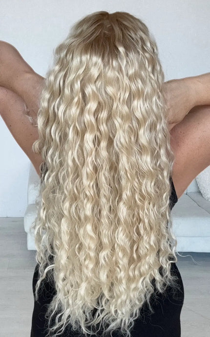 back view of long length light blonde curly hair with slightly darker blonde root, creamy blonde overall tone, with heat safe hair and glueless lace front cap.