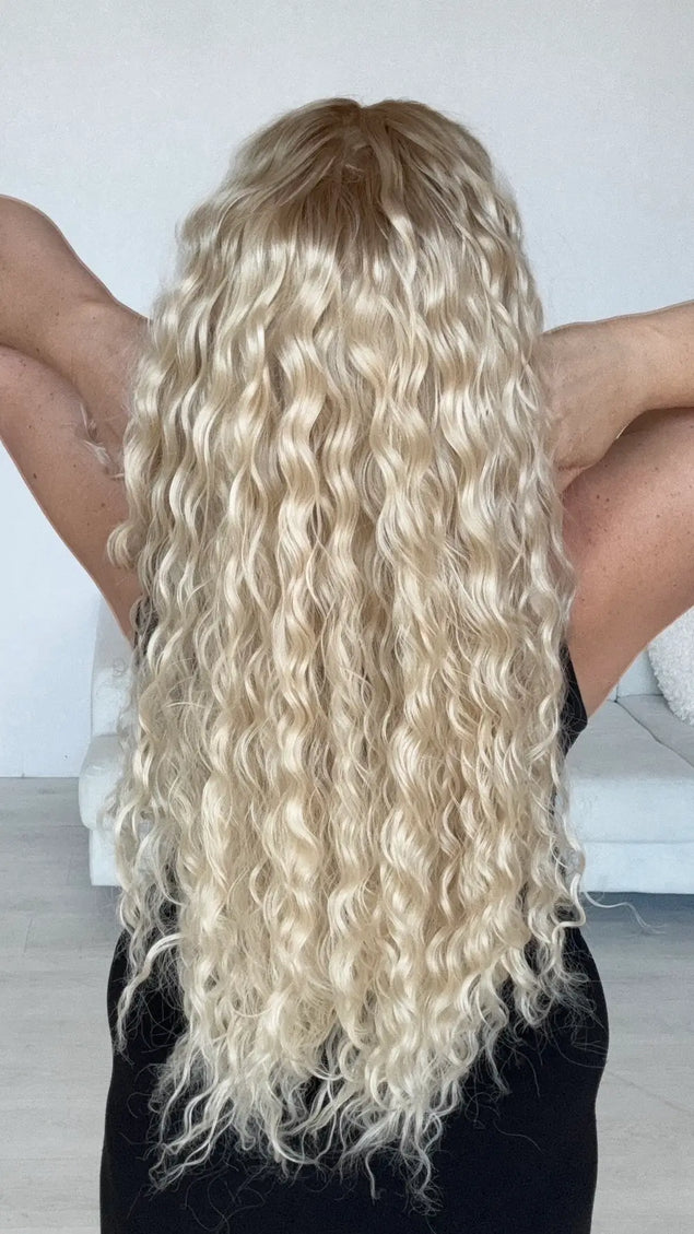 back view of long length light blonde curly hair with slightly darker blonde root, creamy blonde overall tone, with heat safe hair and glueless lace front cap.