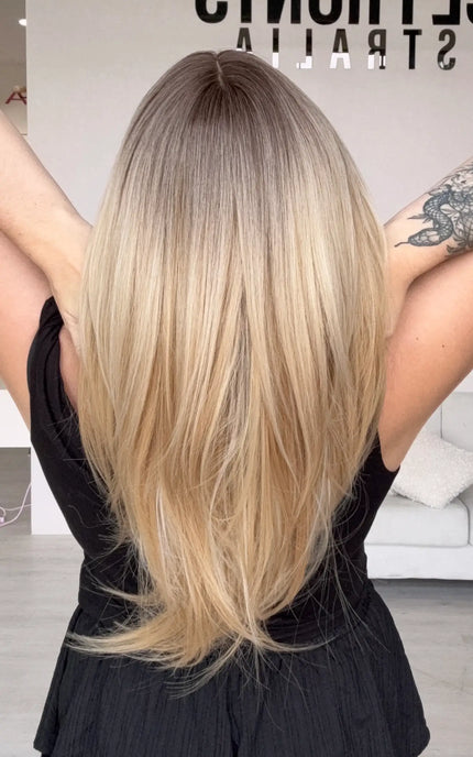 a back view of medium-long length warm blonde hair with blended brunette root, showing layers throughout, middle part and wispy end cut.