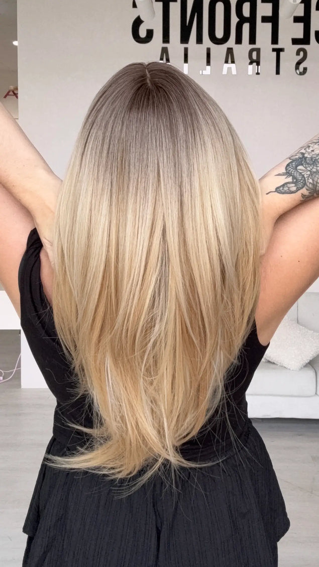 a back view of medium-long length warm blonde hair with blended brunette root, showing layers throughout, middle part and wispy end cut.