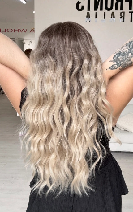 a back view holding the long blonde beachy wave style hair. featuring a glueless cap with adjustable straps.