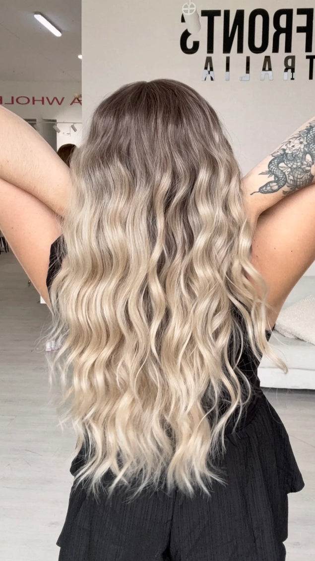 a back view holding the long blonde beachy wave style hair. featuring a glueless cap with adjustable straps.