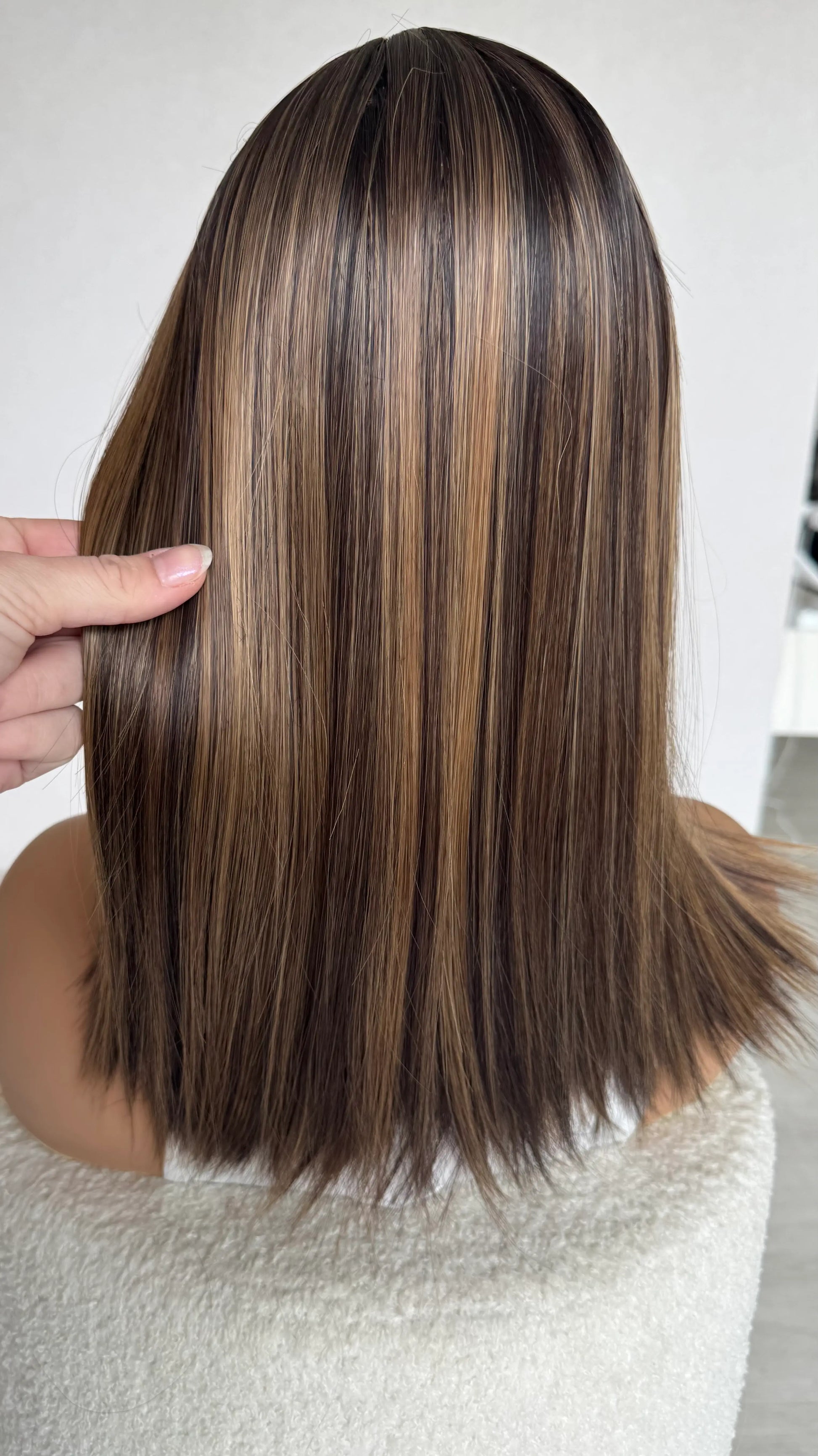 long bob from behind, holding hair with highlights throughout.