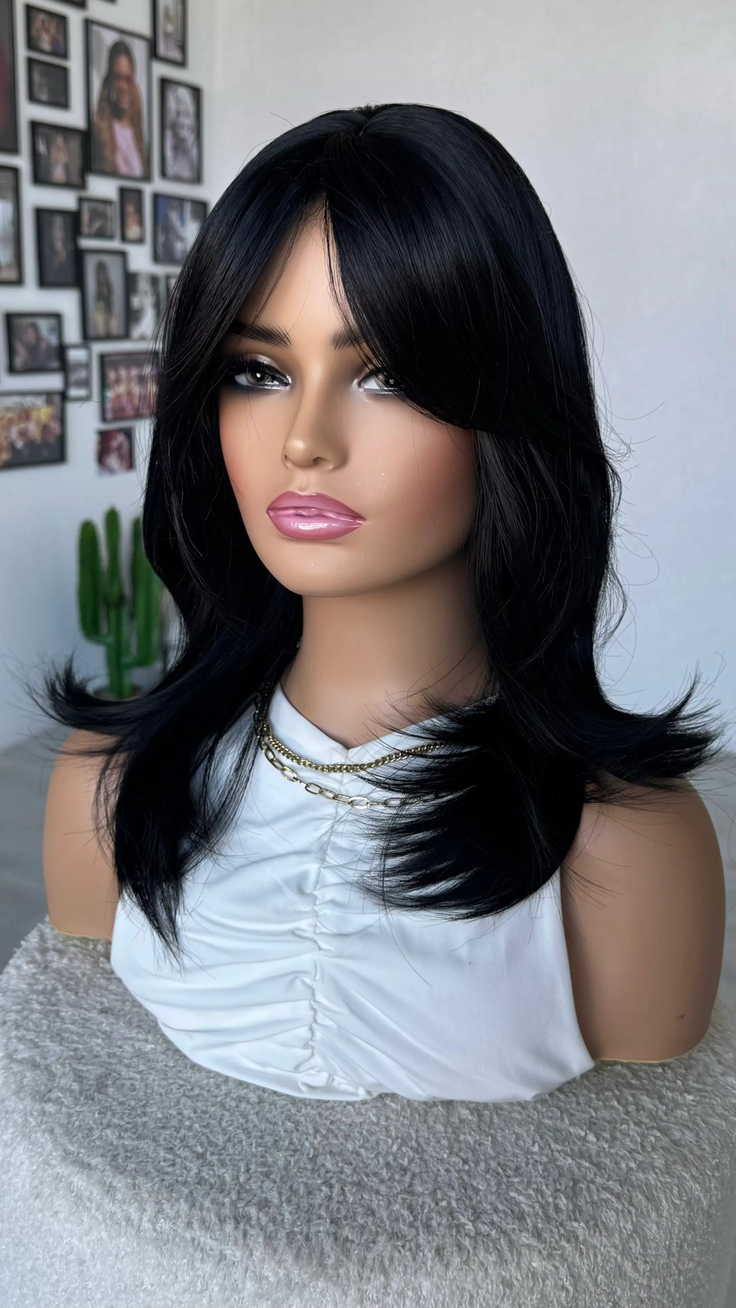 Mannequin head with black wig on a white background, black layered wig with bangs, middle part.