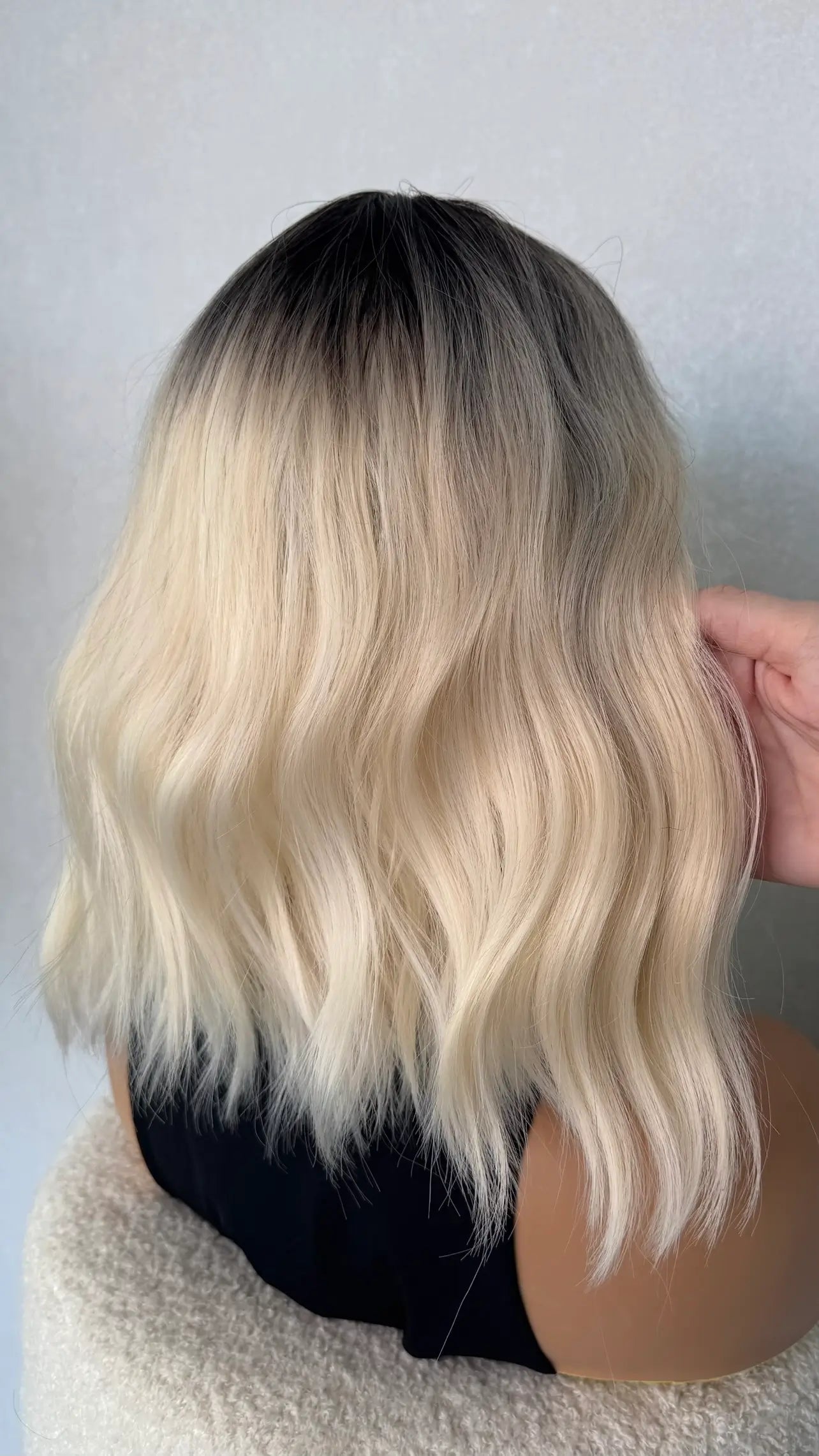 back view of selena blonde synthetic wig. white blonde with dark root.