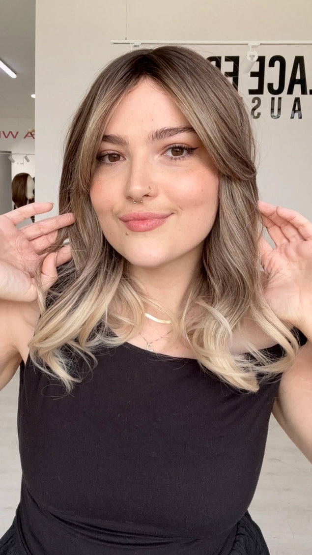 front view holding the hair, dark cool root to ash blonde mids and platinum ends, slight curl on ends. middle part with long curtain bang fringe parted to the side.