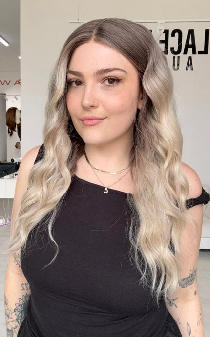 wavy cool toned blonde, dark blonde root to light blonde ends, hoint of rosy tone. middle part with realistic hairline and glueless wig cap.