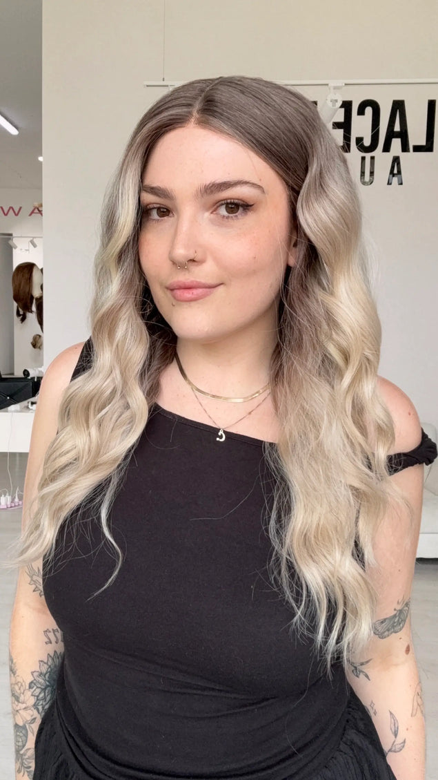 wavy cool toned blonde, dark blonde root to light blonde ends, hoint of rosy tone. middle part with realistic hairline and glueless wig cap.