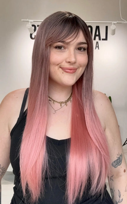 Beginner Friendly long pink synthetic wig with fringe parted to the side and dark roots.