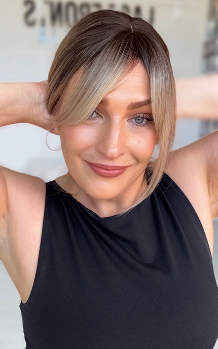 smiling women holding hair back with a few peices falling around her face for shaping, darker brunette root to multi toned blonde ends.