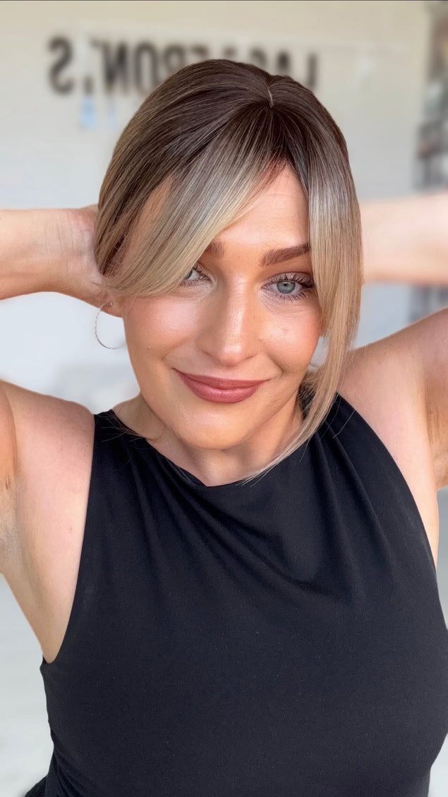 smiling women holding hair back with a few peices falling around her face for shaping, darker brunette root to multi toned blonde ends.