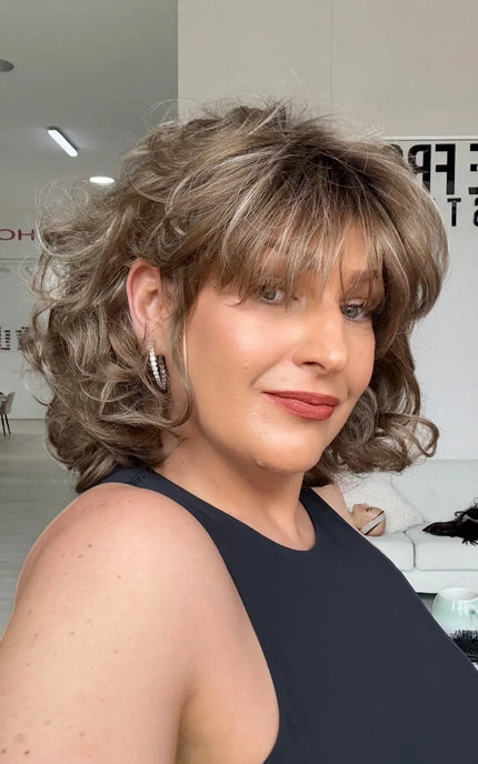 left side view showing bob length, tight curled hair with wispy long fringe and layers throughout, soft light brown colour with blonde highlights throughout for natural look.