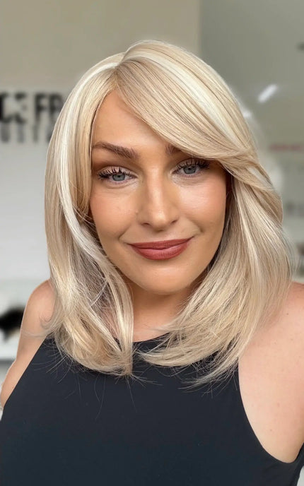 light creamy blonde long bob with bangs styled to the right hand side, soft highlights throughout and layers for movement. glueless wig cap design