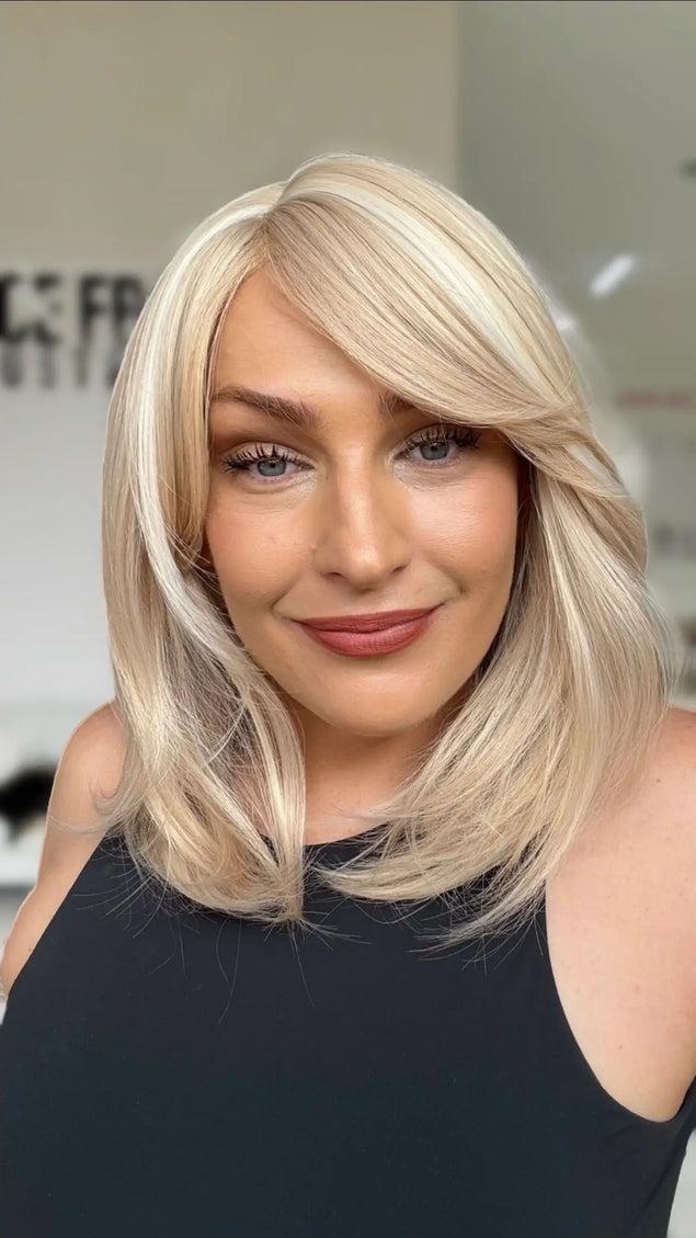 light creamy blonde long bob with bangs styled to the right hand side, soft highlights throughout and layers for movement. glueless wig cap design