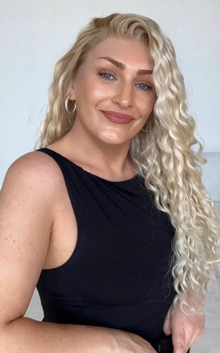 a light creamy blonde curly hair wig with a realistic lace front hairline, long length curly hair with left side, changeable part and darker blonde shadow root.
