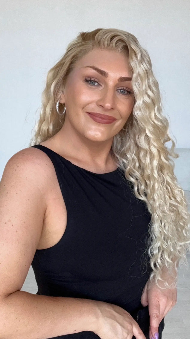 a light creamy blonde curly hair wig with a realistic lace front hairline, long length curly hair with left side, changeable part and darker blonde shadow root.