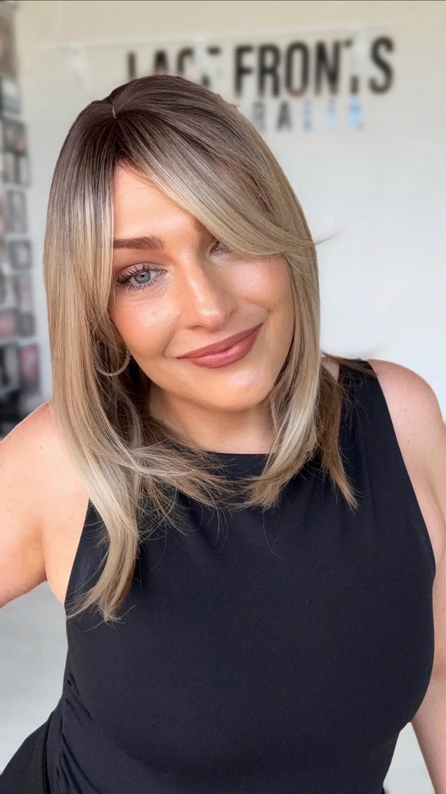 multi toned blonde layered long bob with curtain bangs and layers around face. multi toned slight warm blonde with soft brunette shadow root.