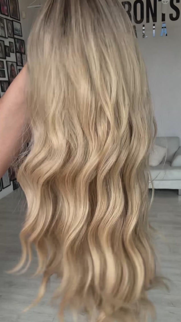 warm buttery blonde wavy hair with darker root, soft wavy heat safe hair with glueless cap for easy everyday wear. middle part with fringe.