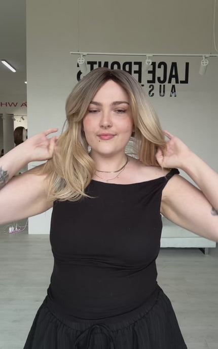 a layered warm blonde ombre hair with a soft brunette root, middle part and curtain bangs parted to the side, can be worn up or down. can be heat styled, can be worn glueless.